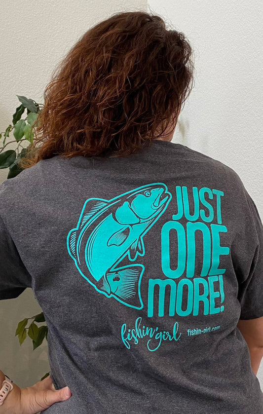 Dark gray t-shirt with teal design. A redfish to the left and the words "Just One More!" to the right with the Fishin' Girl logo and web address beneath it.